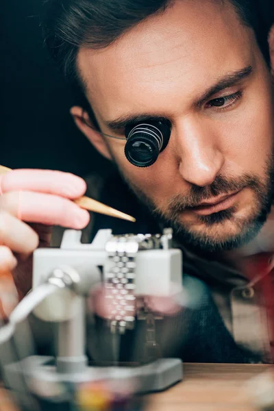 Selective focus of handsome clockmaker working with wristwatch on movement holder isolated on black — Stock Photo