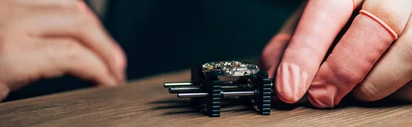 Cropped view of watchmaker working with watch on movement holder at table, panoramic shot — Stock Photo