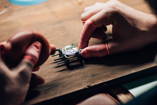 Vista recortada del relojero utilizando soplador para reloj de pulsera en el soporte de movimiento en la mesa - foto de stock