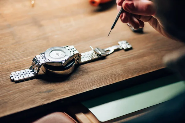 Vista ritagliata dell'orologiaio che lavora con cacciavite e orologio da polso sul supporto sul tavolo — Foto stock