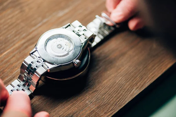 Selective focus of watchmaler holding wristwatch on stand on wooden table — Stock Photo