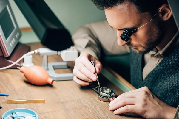 Side view of watchmaker in eyeglass loupe working with wristwatch by equipment on table — Stock Photo