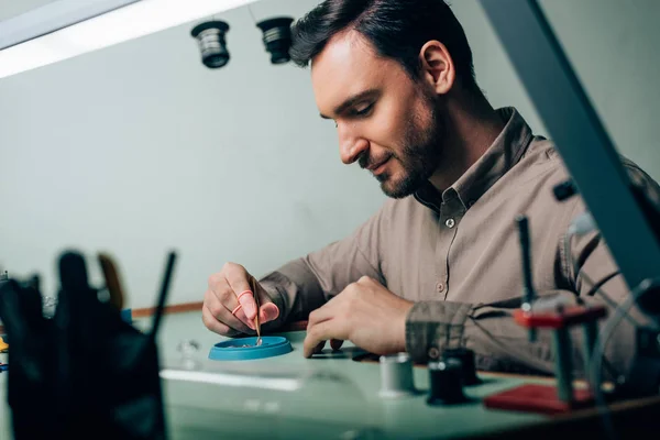 Vue latérale de l'horloger travaillant avec une pince à épiler et un plateau à outils à la table — Photo de stock