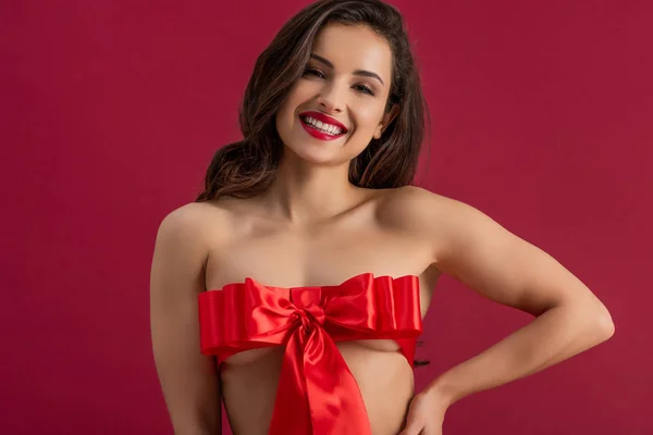 Seductive girl, wrapped in red satin ribbon with bow, smiling at camera isolated on red — Stock Photo