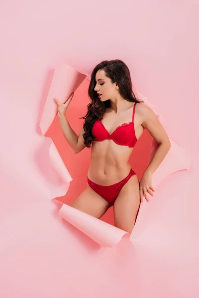 Sensual girl in red lingerie standing in paper hole on pink background — Stock Photo