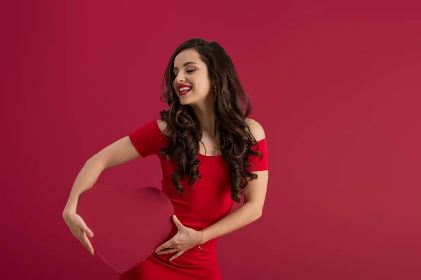 Sexy, elegantes Mädchen mit Papierherz, während es mit geschlossenen Augen auf Rot lächelt — Stockfoto