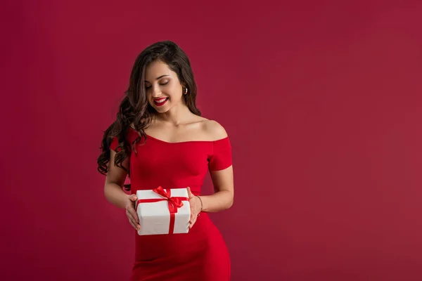 Sexy, elegantes Mädchen lächelt, während sie Geschenkbox isoliert auf rot hält — Stockfoto