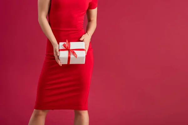 Обрезанный вид сексуальной, элегантной девушки с подарочной коробкой, стоя изолированы на красный — стоковое фото