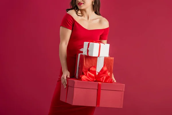 Vista recortada de sexy, elegante chica sosteniendo cajas de regalo mientras está de pie aislado en rojo - foto de stock