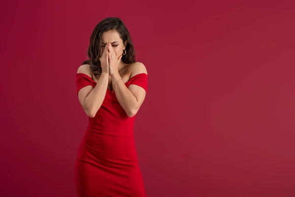 Засмучена, елегантна дівчина закриває обличчя руками, стоячи ізольовано на червоному — стокове фото
