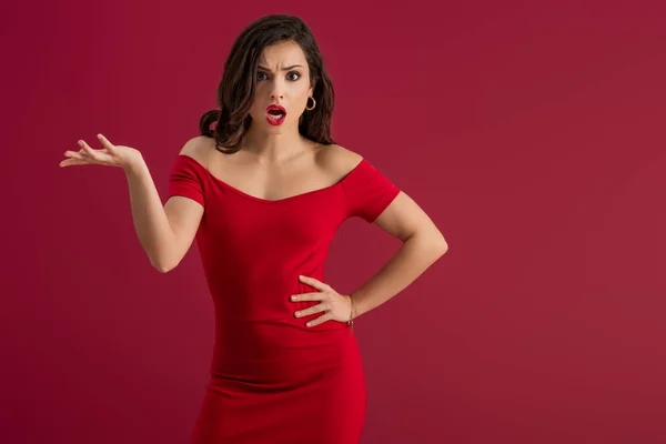 Irritated, elegant girl screaming at camera while standing with open arm isolated on red — Stock Photo