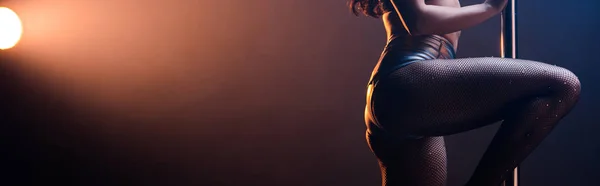 Panoramic shot of stripper dancing near pole on blue with orange lighting — Stock Photo