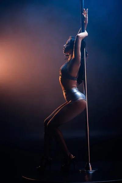 Вид сбоку на сексуальную стриптизершу в нижнем белье, стоящую возле столба на синем и оранжевом — стоковое фото