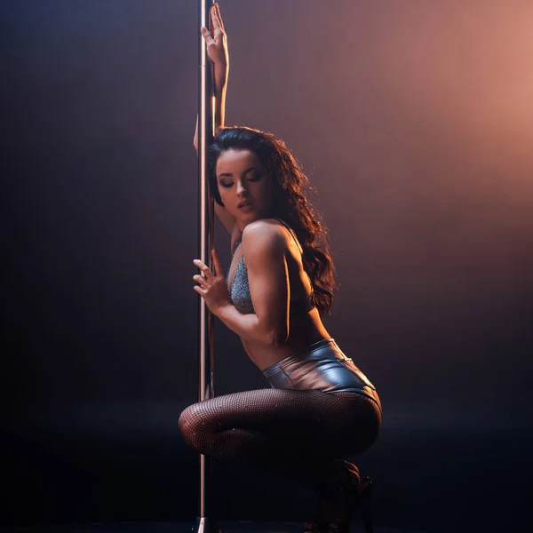 Attractive stripper in underwear sitting near pole on black and orange — Stock Photo