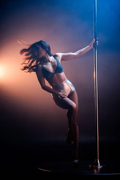 Sexy woman in undrewear dancing striptease near pylon on blue with orange lighting — Stock Photo