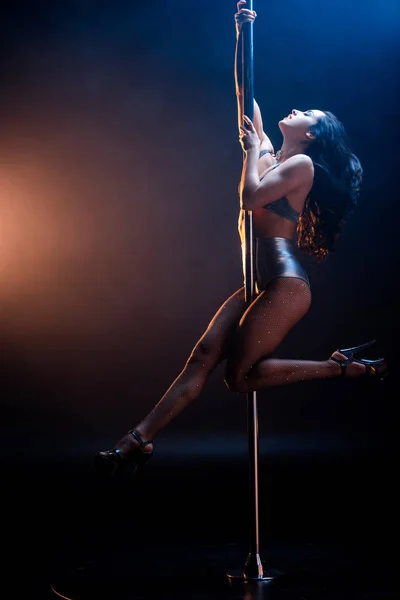 Seductora stripper en ropa interior bailando striptease cerca de pilón en azul y naranja - foto de stock