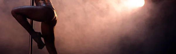 Панорамний знімок стриптизерки в рибальських колготках танцює стриптиз біля пілона на чорному з димом — стокове фото