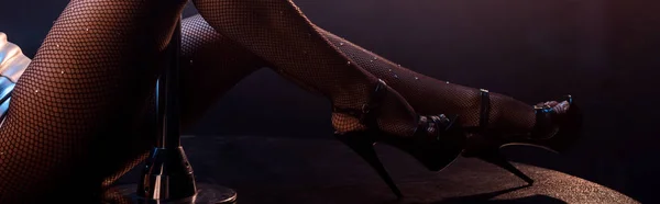 Panoramaaufnahme einer sexy Stripperin in Netzstrumpfhose und High Heels auf Schwarz — Stockfoto