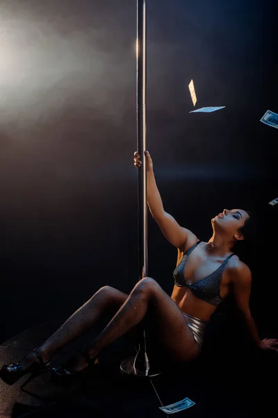 Dollar banknotes falling near sexy stripper pole dancing on black with smoke — Stock Photo