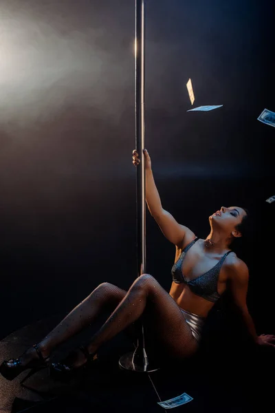 Dollar banknotes falling near sexy stripper pole dancing on black with smoke — Stock Photo