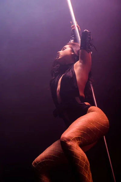 Low angle view of sexy young stripper with closed eyes pole dancing on blue — Stock Photo