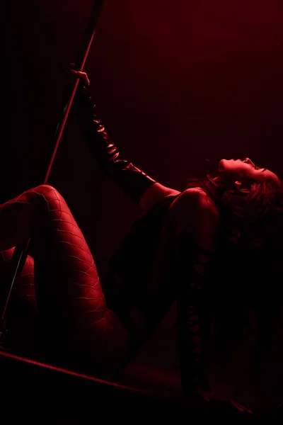 Red lighting on seductive stripper dancing near pylon on black with red lighting — Stock Photo