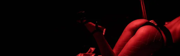 Plano panorámico de mujer apasionada bailando striptease cerca de billetes de dólar aislados en negro con iluminación roja - foto de stock