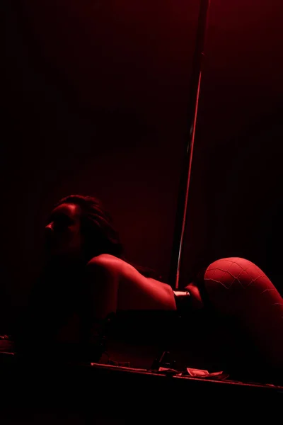 Femme passionnée dansant strip-tease près de billets de dollar sur noir avec éclairage rouge — Photo de stock