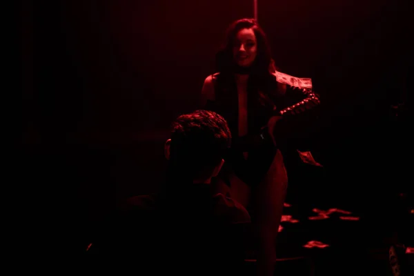 Back view of man standing near smiling stripper on black with red lighting — Stock Photo