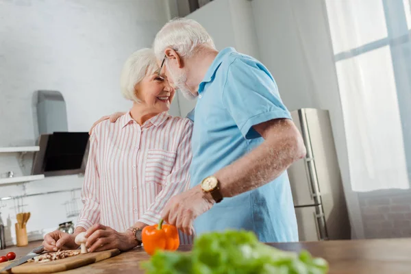 Foco seletivo de casal sênior sorridente olhando um para o outro enquanto cozinha na cozinha — Fotografia de Stock