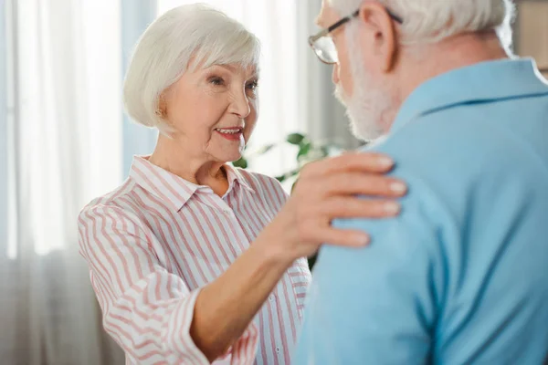 Выборочный фокус улыбающейся пожилой женщины, обнимающей мужа дома — стоковое фото