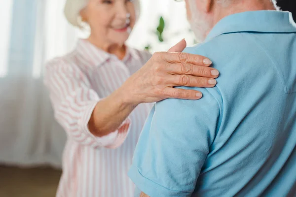 Selektiver Fokus einer lächelnden Seniorin, die Ehemann zu Hause an der Schulter berührt — Stockfoto