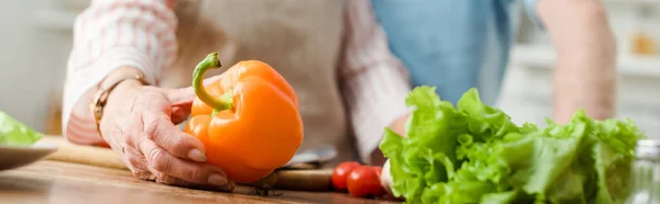 Cropped view of woman holding bell pepper while cooking by man in kitchen, panoramic shot — Stock Photo