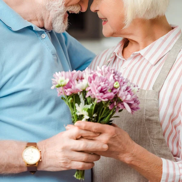 Vista recortada de la pareja de ancianos sonriéndose y sosteniendo ramo de crisantemos - foto de stock