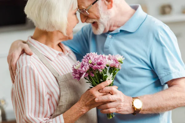 Selective focus of senior man hugging smiling wife with bouquet of chrysanthemums — Stock Photo
