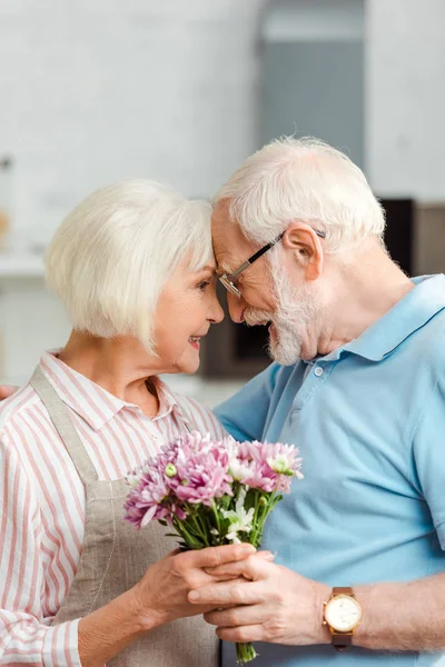Side view of senior couple holding bouquet and smiling at each other at home — Stock Photo