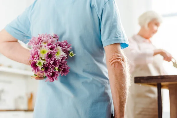 Focus selettivo dell'uomo nascondendo bouquet con moglie dal tavolo della cucina sullo sfondo — Foto stock