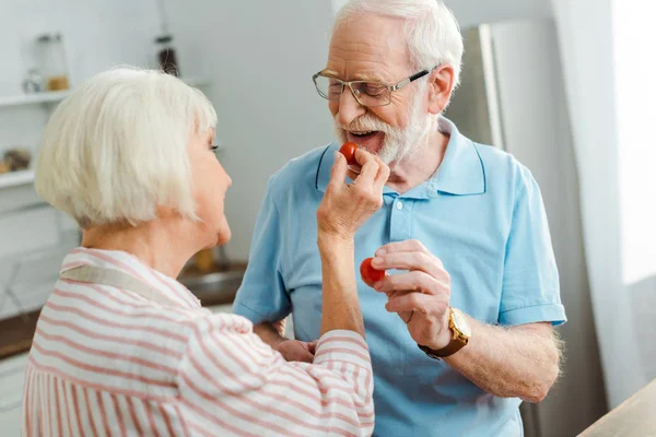Seniorenpaar hält reife Kirschtomaten in der Küche — Stockfoto