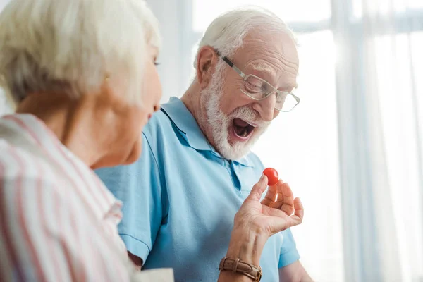 Concentration sélective de la femme âgée donnant tomate cerise au mari dans la cuisine — Photo de stock