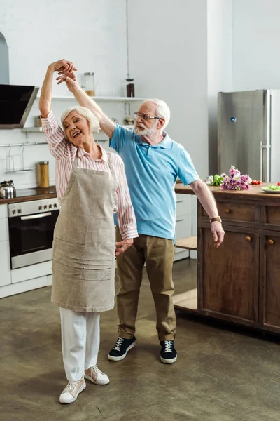 Senior homme dansant avec femme souriante dans tablier dans la cuisine — Photo de stock