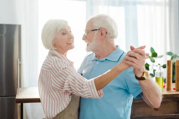 Seitenansicht eines lächelnden Senioren-Paares, das sich beim Tanzen in der Küche anschaut — Stockfoto