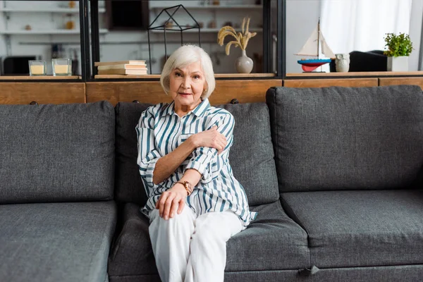 Seniorin schaut in Kamera, während sie auf Couch im Wohnzimmer sitzt — Stockfoto