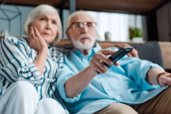 Selective focus of focused senior couple watching tv on couch in living room — Stock Photo