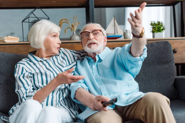 Selective focus of senior man gesturing while watching tv with wife on couch in living room — Stock Photo