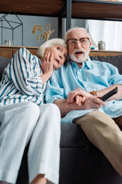 Enfoque selectivo de la impactada pareja mayor viendo la televisión en el sofá en casa - foto de stock