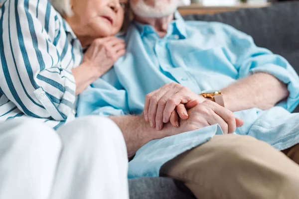 Selective focus of elderly couple holding hands while sitting on couch — Stock Photo