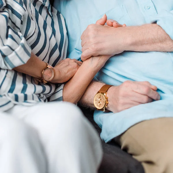 Обрезанный вид пожилого мужчины, держащего жену за руку на диване — стоковое фото