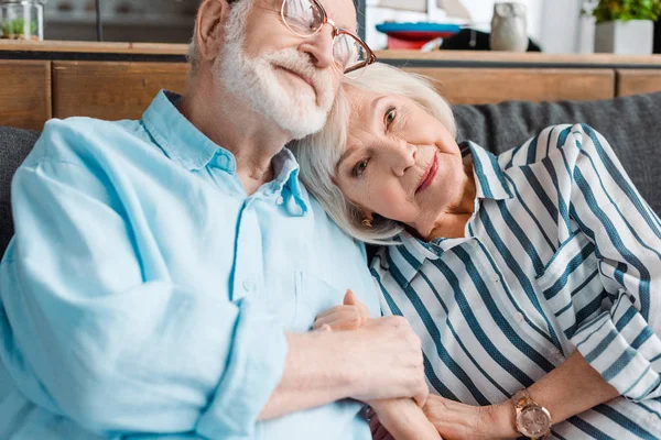 Seniorin blickt in Kamera, während sie Mann auf Sofa an der Hand hält — Stockfoto