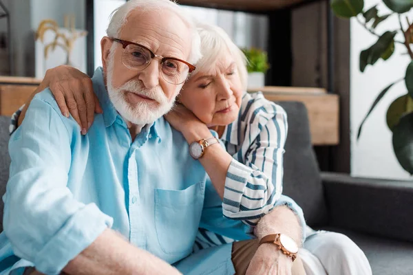 Selektiver Fokus eines älteren Mannes, der auf der Couch in die Kamera seiner Frau blickt — Stockfoto
