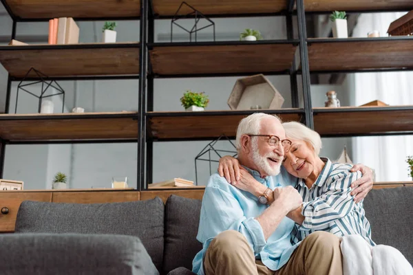 Low angle view of smiling senior man embracing wife on couch in living room — Stock Photo